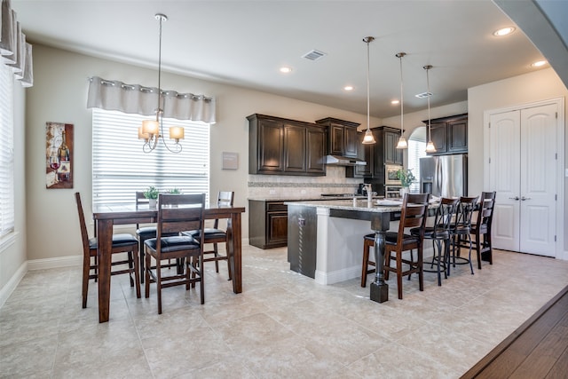 kitchen with stainless steel fridge with ice dispenser, backsplash, decorative light fixtures, a breakfast bar area, and a center island with sink