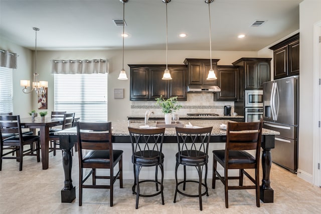 kitchen featuring light stone countertops, hanging light fixtures, appliances with stainless steel finishes, and an island with sink