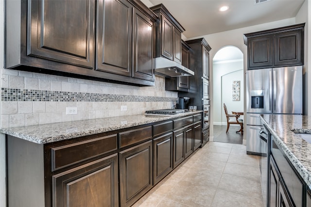 kitchen featuring stainless steel appliances, light stone counters, backsplash, dark brown cabinets, and light tile patterned flooring