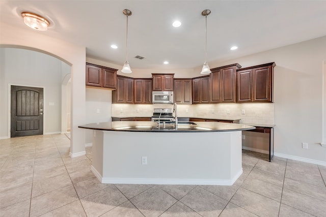 kitchen featuring backsplash, dark brown cabinetry, stainless steel appliances, and a kitchen island with sink