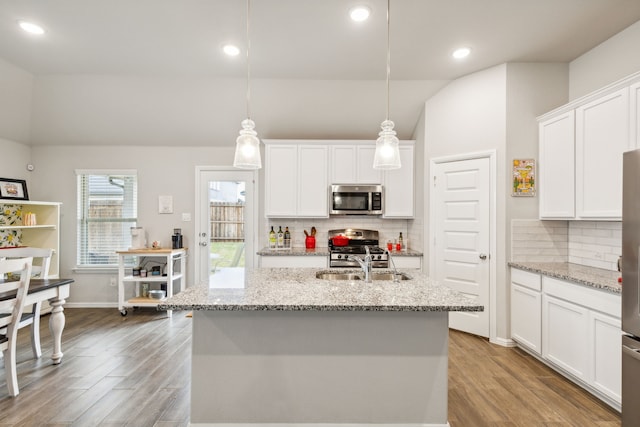 kitchen with a center island with sink, hanging light fixtures, light hardwood / wood-style flooring, white cabinetry, and stainless steel appliances