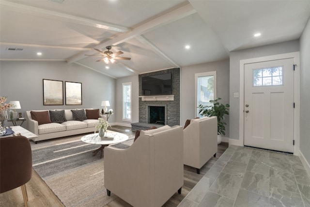 living room featuring plenty of natural light, ceiling fan, a large fireplace, and lofted ceiling with beams