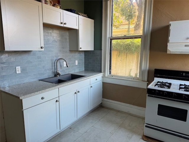 kitchen with a wealth of natural light, gas range gas stove, sink, light stone countertops, and white cabinets