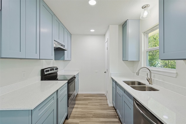 kitchen featuring appliances with stainless steel finishes, light stone counters, a textured ceiling, sink, and light hardwood / wood-style flooring