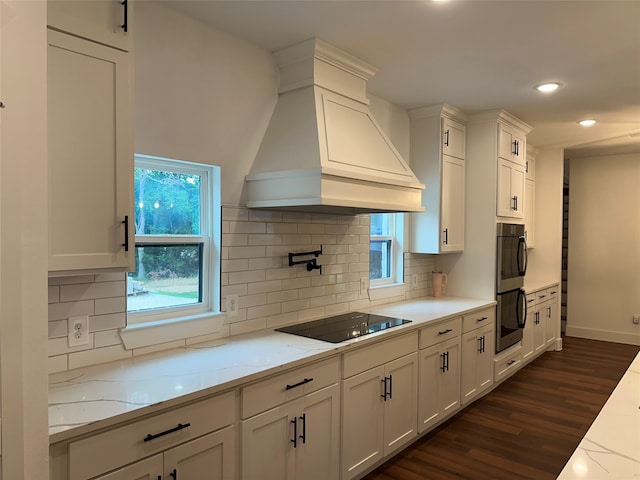 kitchen featuring light stone counters, custom range hood, black electric cooktop, dark hardwood / wood-style floors, and white cabinetry