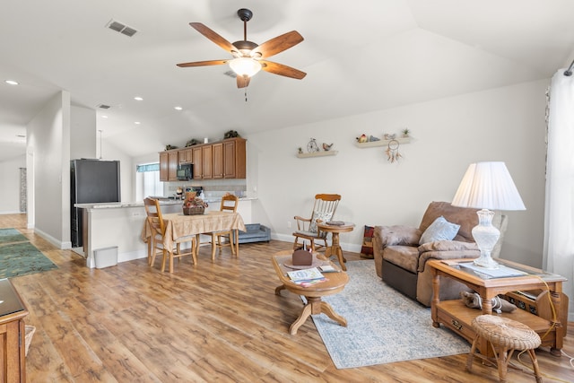 living room with ceiling fan, light hardwood / wood-style flooring, and vaulted ceiling