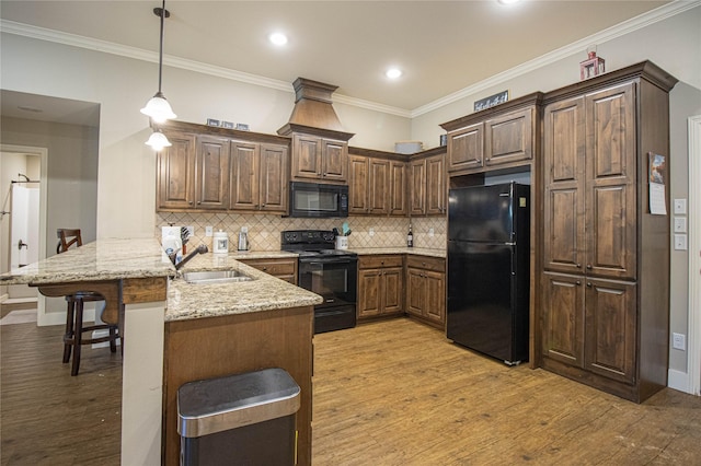 kitchen featuring kitchen peninsula, a breakfast bar, black appliances, pendant lighting, and light hardwood / wood-style floors