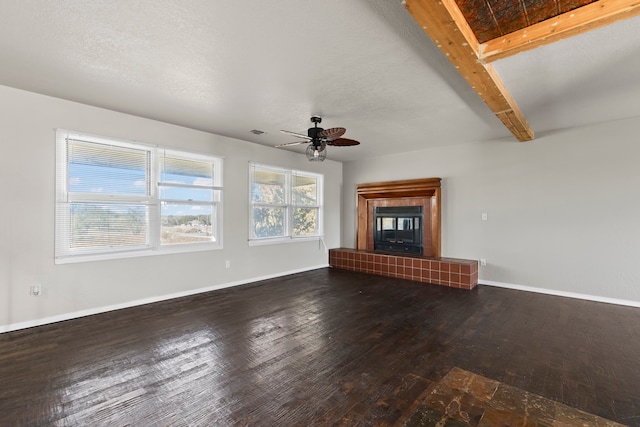 unfurnished living room with a fireplace, a textured ceiling, ceiling fan, beamed ceiling, and dark hardwood / wood-style floors