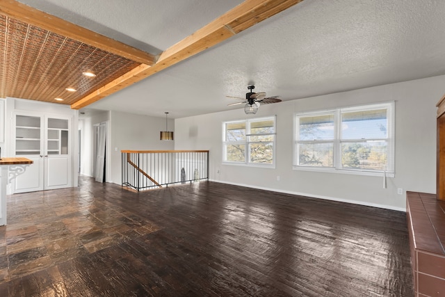 unfurnished living room featuring beamed ceiling, dark hardwood / wood-style floors, ceiling fan, and a textured ceiling