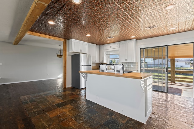 kitchen with stainless steel refrigerator, white cabinetry, a center island, tasteful backsplash, and wooden counters