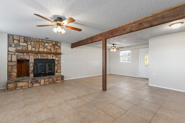 unfurnished living room with beam ceiling, a stone fireplace, ceiling fan, and a textured ceiling