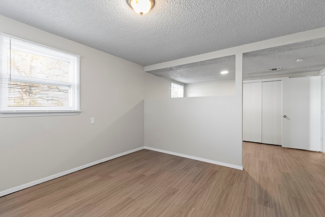 basement with plenty of natural light, light hardwood / wood-style floors, and a textured ceiling