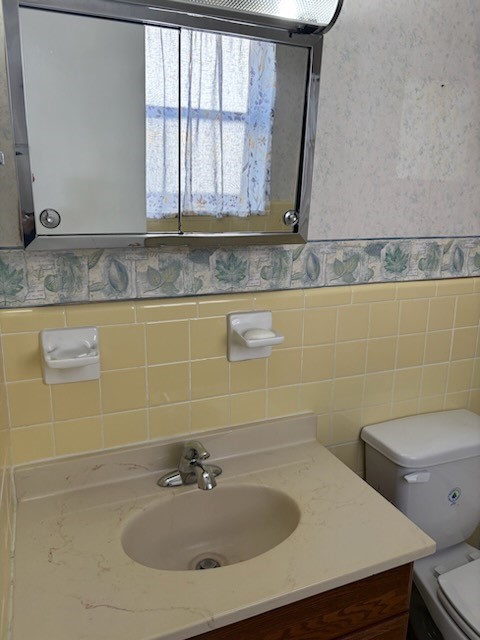 bathroom featuring vanity, toilet, and tile walls