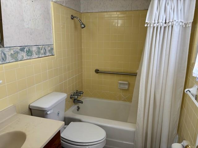 full bathroom featuring vanity, toilet, shower / bathtub combination with curtain, and tile walls