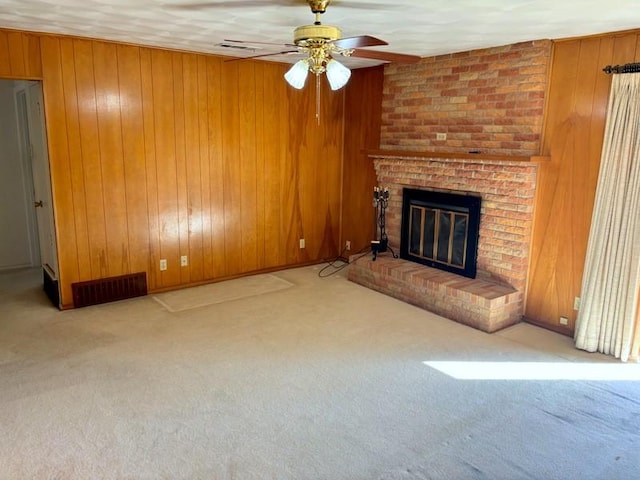 unfurnished living room featuring light colored carpet, a brick fireplace, ceiling fan, and wooden walls