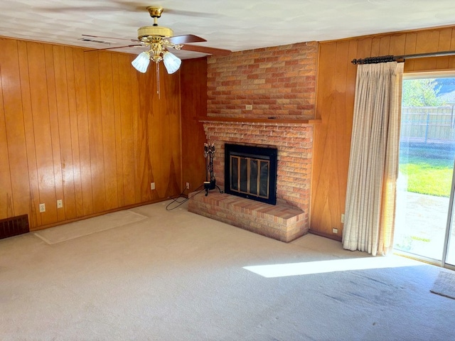 unfurnished living room featuring wood walls, ceiling fan, light colored carpet, and a brick fireplace