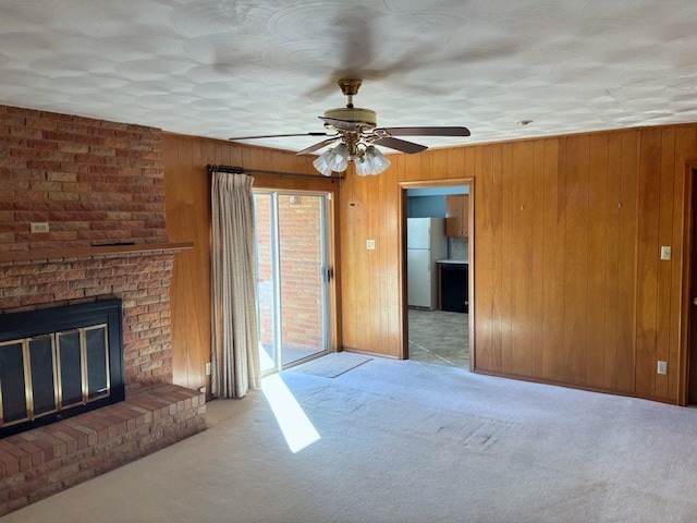 unfurnished living room with ceiling fan, wood walls, light colored carpet, and a fireplace