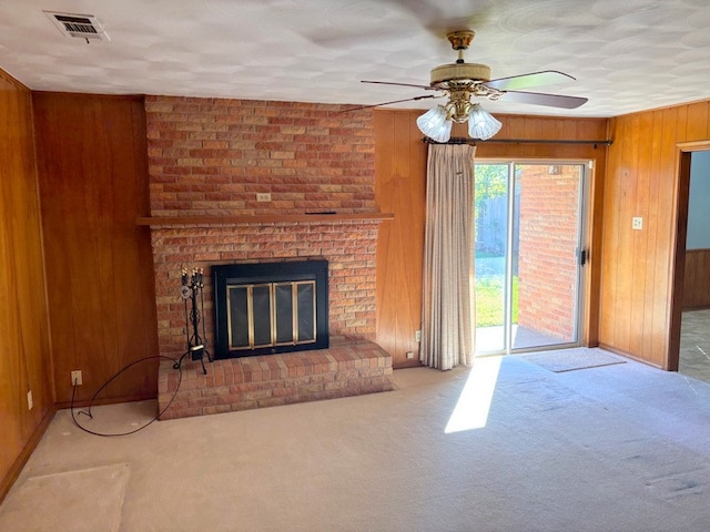 unfurnished living room featuring carpet, a brick fireplace, ceiling fan, and wooden walls