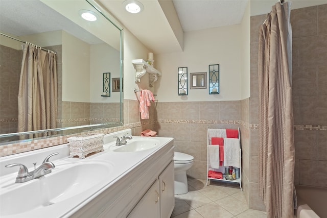 bathroom with tile patterned flooring, a textured ceiling, toilet, vanity, and tile walls