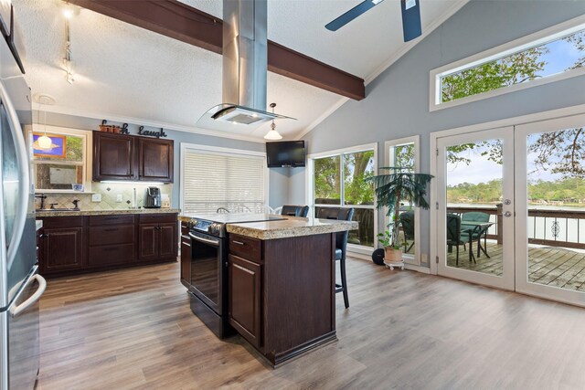 kitchen with black / electric stove, light hardwood / wood-style flooring, a kitchen island, and a healthy amount of sunlight