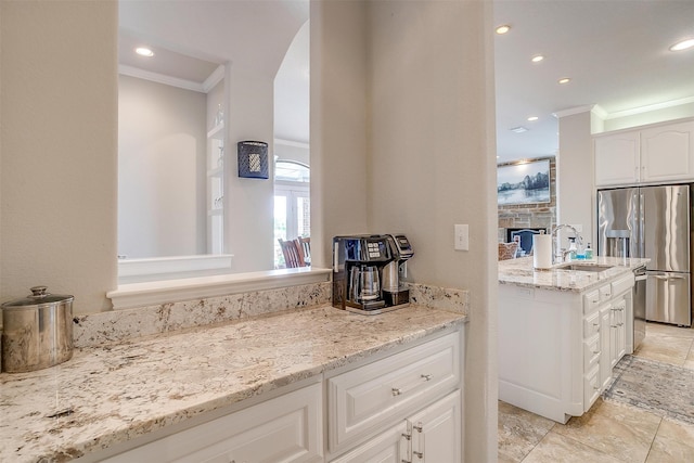 kitchen with light stone countertops, sink, stainless steel fridge with ice dispenser, crown molding, and white cabinets