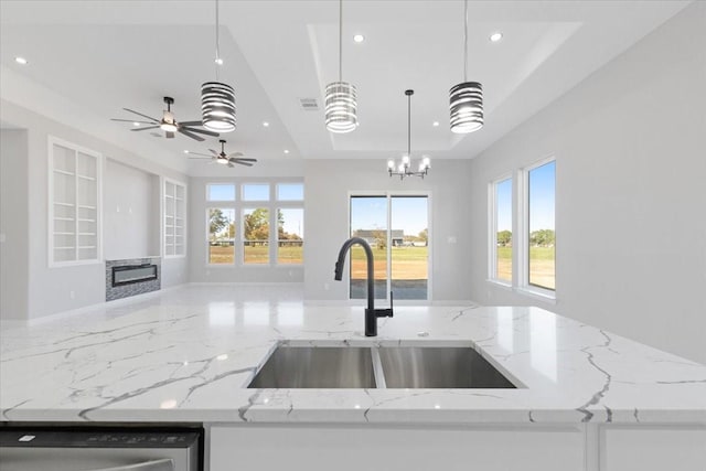 kitchen featuring sink, light stone counters, a tray ceiling, decorative light fixtures, and stainless steel dishwasher