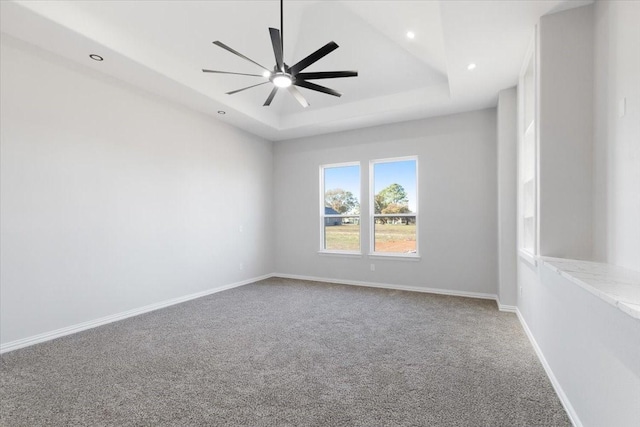 carpeted spare room with a tray ceiling and ceiling fan