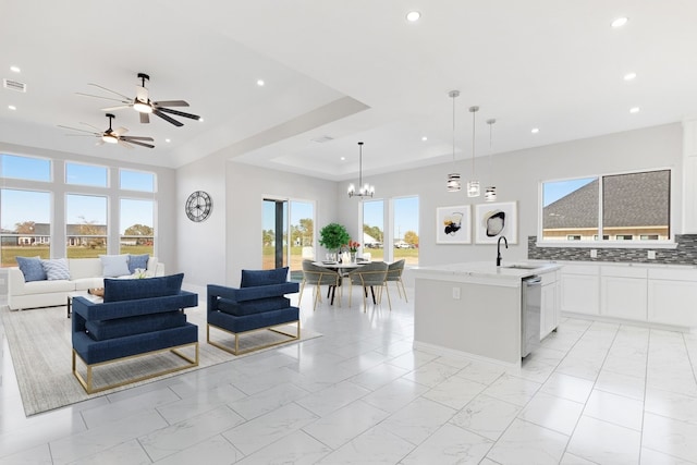 interior space with a center island with sink, decorative light fixtures, sink, a raised ceiling, and white cabinets