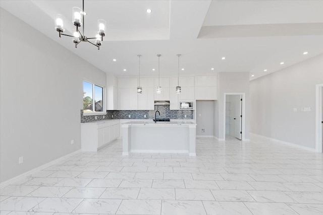 kitchen featuring a kitchen island with sink, hanging light fixtures, sink, tasteful backsplash, and white cabinets