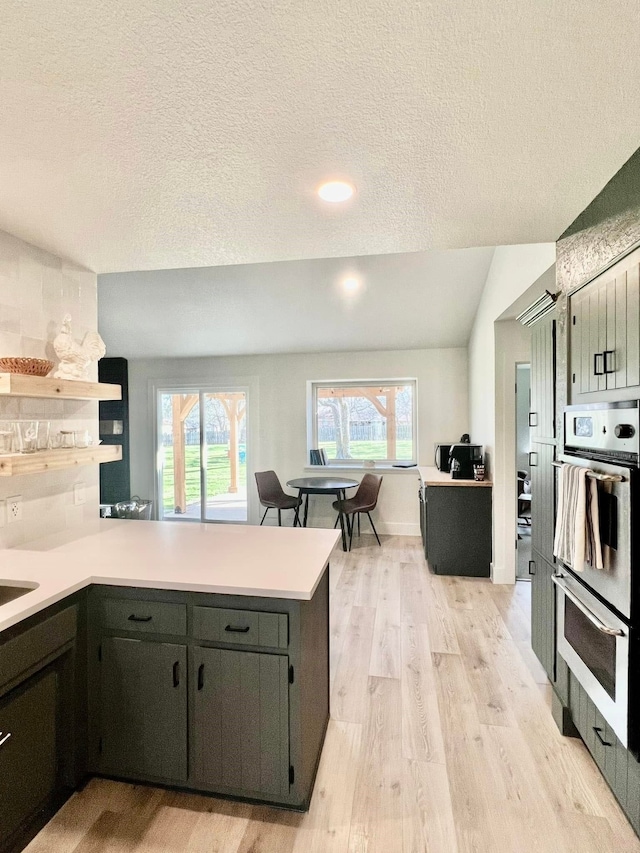 kitchen with a peninsula, light wood-style flooring, light countertops, a textured ceiling, and double oven