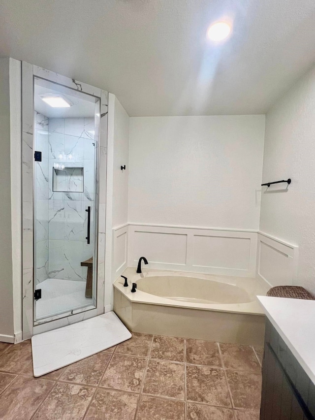 full bath with a marble finish shower, a decorative wall, a garden tub, and a wainscoted wall