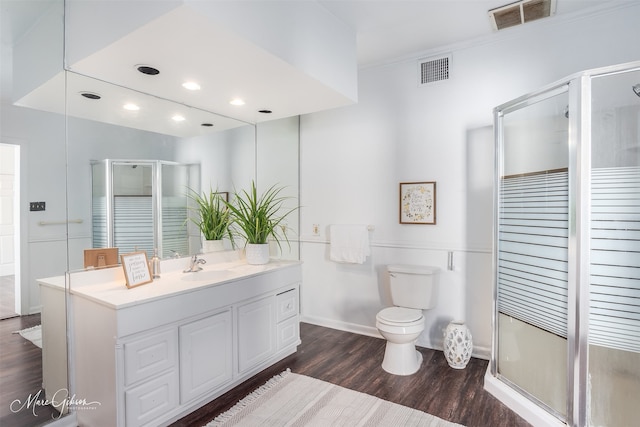 bathroom featuring wood-type flooring, toilet, a shower with door, vanity, and ornamental molding