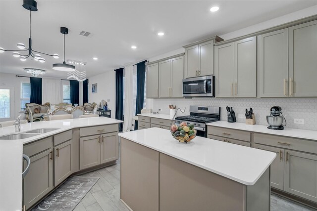 kitchen with gray cabinetry, sink, stainless steel appliances, pendant lighting, and a kitchen island