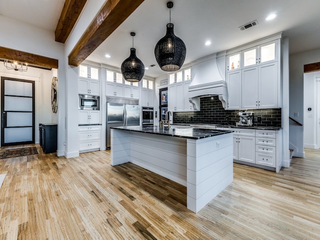 kitchen with white cabinets, a kitchen island with sink, built in appliances, custom range hood, and beam ceiling