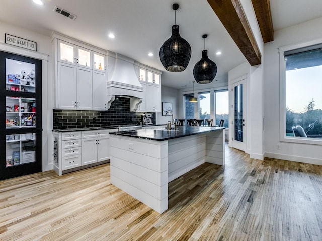 kitchen with custom exhaust hood, white cabinetry, a kitchen island with sink, and decorative light fixtures