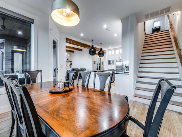 dining room featuring sink, beam ceiling, and light wood-type flooring