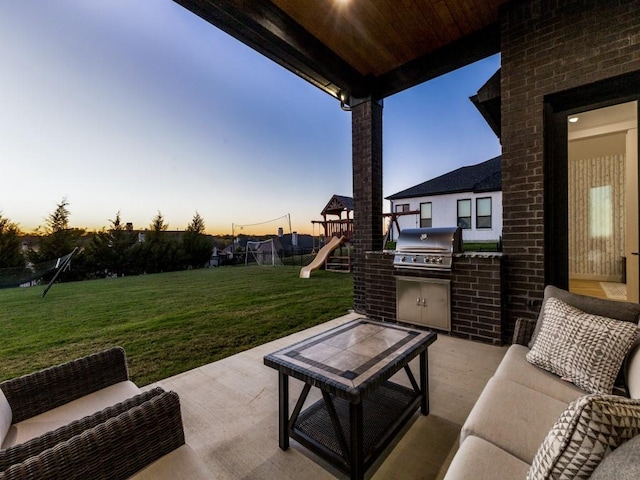 patio terrace at dusk with a playground, a lawn, a trampoline, exterior kitchen, and grilling area