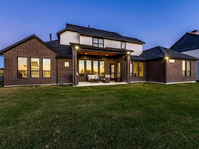 back house at dusk with an outdoor hangout area, a patio area, ceiling fan, and a lawn