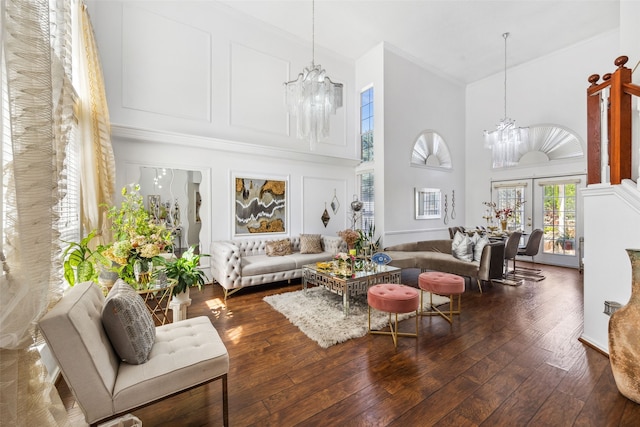 living room with dark wood-type flooring, french doors, crown molding, a towering ceiling, and a chandelier