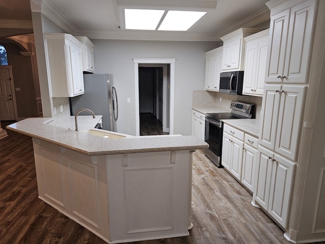 kitchen with a sink, wood finished floors, white cabinetry, appliances with stainless steel finishes, and a peninsula