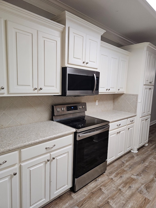 kitchen featuring white cabinets, light wood-type flooring, stainless steel appliances, and ornamental molding