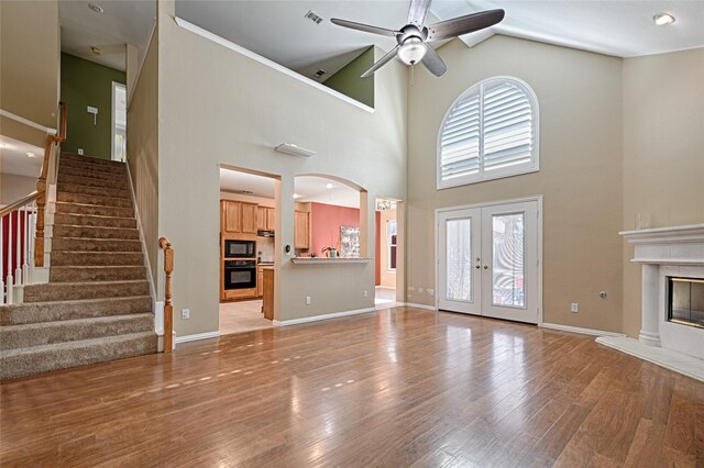 unfurnished living room featuring french doors, light wood-type flooring, high vaulted ceiling, and ceiling fan