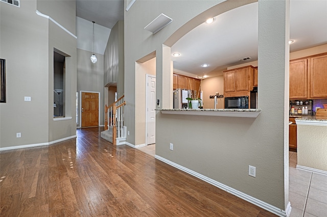 kitchen with light stone countertops, stainless steel fridge, light wood-type flooring, and kitchen peninsula