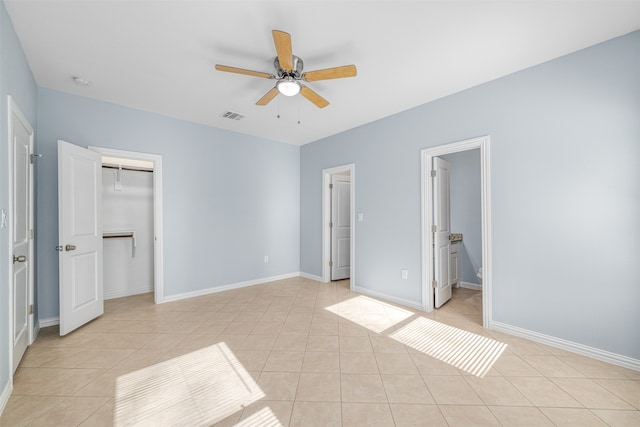 unfurnished bedroom featuring ensuite bathroom, ceiling fan, light tile patterned floors, a spacious closet, and a closet