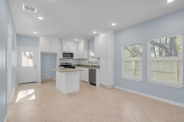 kitchen featuring light stone countertops, appliances with stainless steel finishes, a center island, and a wealth of natural light