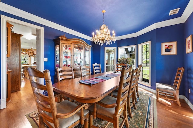 dining space featuring crown molding, an inviting chandelier, visible vents, wood finished floors, and baseboards