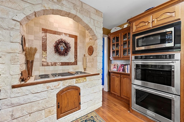 kitchen with glass insert cabinets, light wood-type flooring, light countertops, stainless steel appliances, and brown cabinets