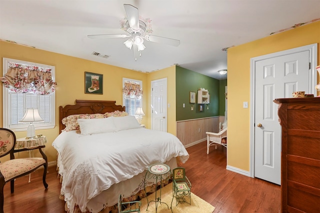 bedroom with ceiling fan, wood walls, wood-type flooring, and multiple windows