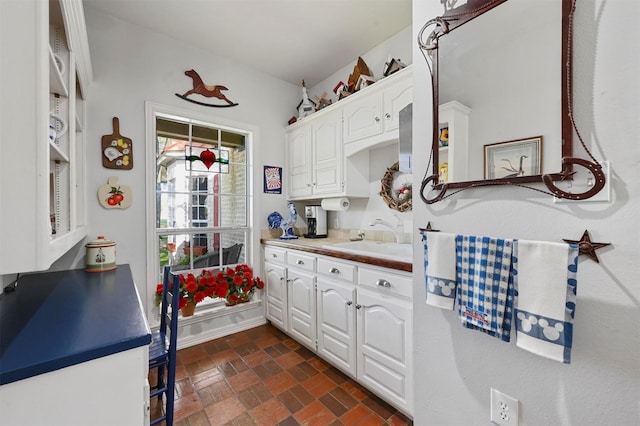 kitchen with baseboards, brick floor, white cabinetry, and a sink