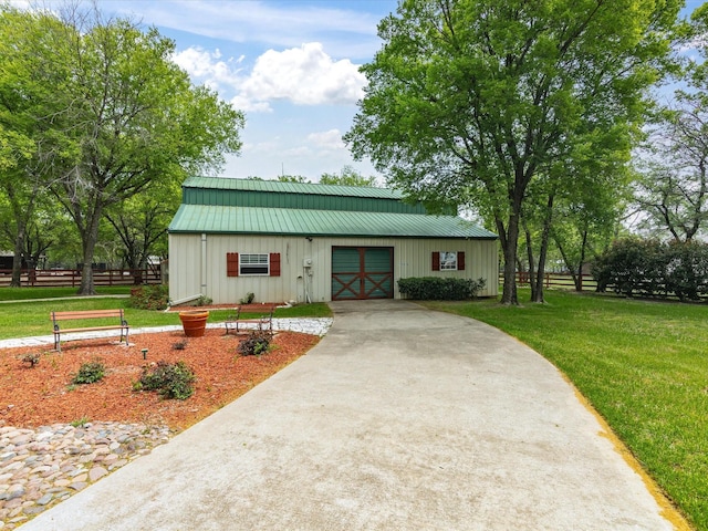 view of front of property featuring an outbuilding, metal roof, a front yard, fence, and driveway